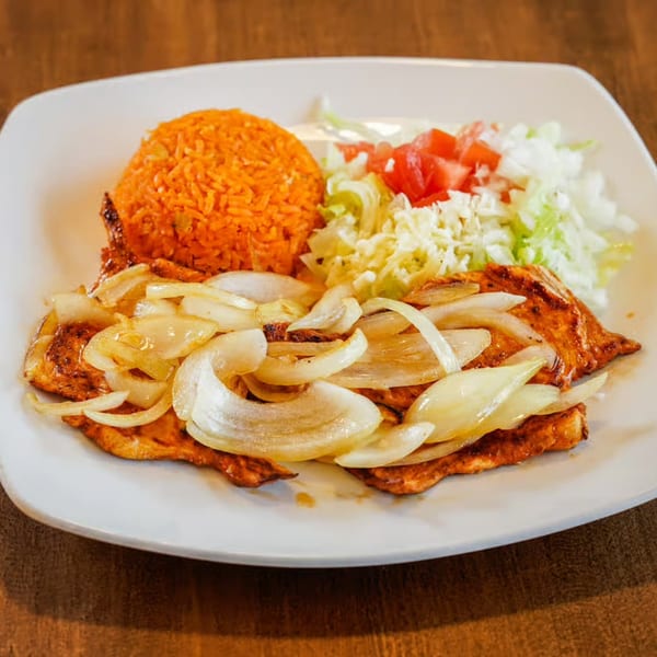 Grilled chicken with sautéed onions, orange rice, and a side salad with tomatoes and cheese.
