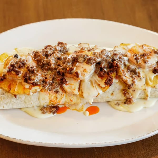 A large burrito covered in melted white cheese, ground meat, and orange sauce on a white plate.