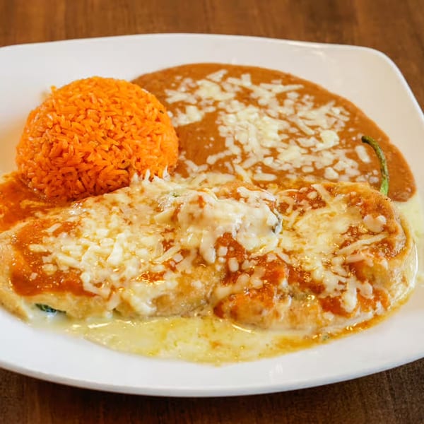 A chile relleno covered in cheese and red sauce, with a side of orange rice and refried beans.