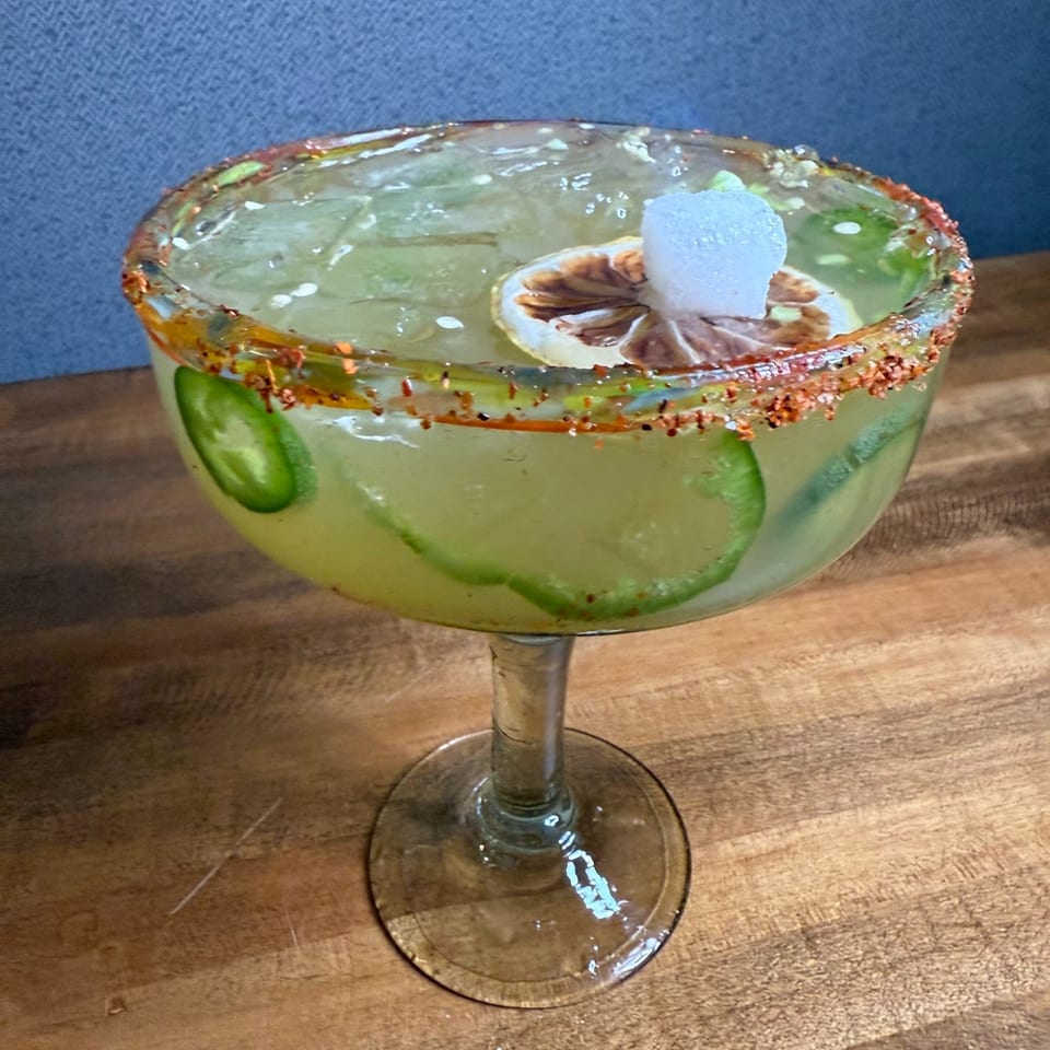 Spicy margarita with jalapeño slices, a lime wheel, and a sugar cube, rimmed with chili salt.