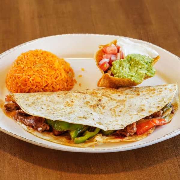 Steak fajita quesadilla with rice, guacamole, pico de gallo, and sour cream on a white plate.