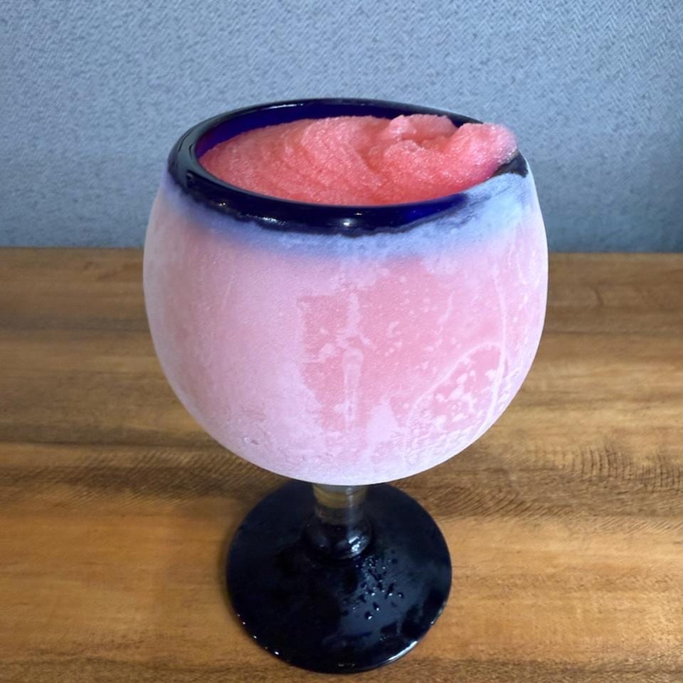 A frosty pink frozen drink in a blue-rimmed glass sits on a wooden table.
